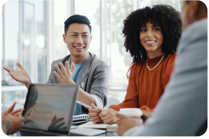 Group of diverse colleagues engaged in a collaborative meeting, with two individuals smiling and discussing ideas in a bright, modern office setting.